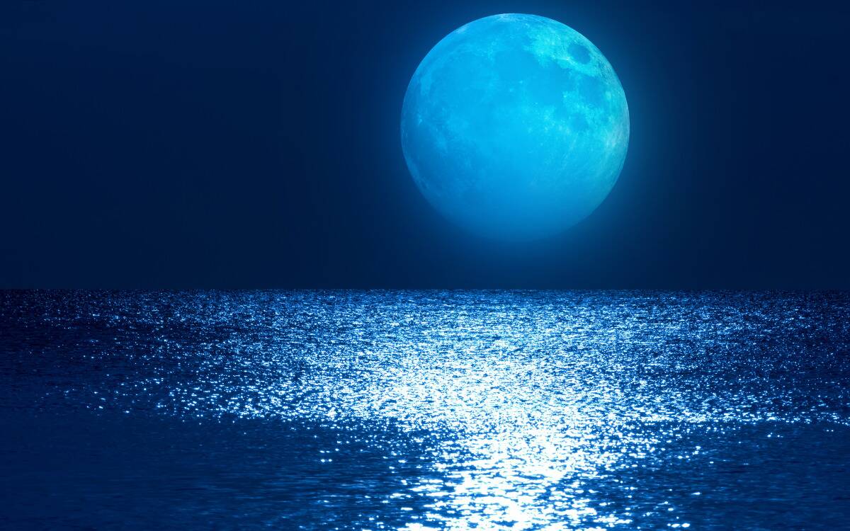 A large blue moon rising above a shimmering body of water.