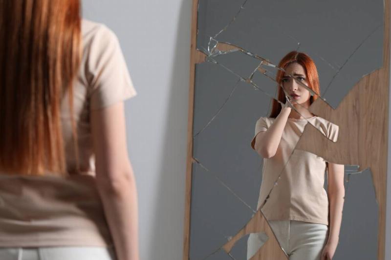 A woman looking at herself in a shattered mirror.