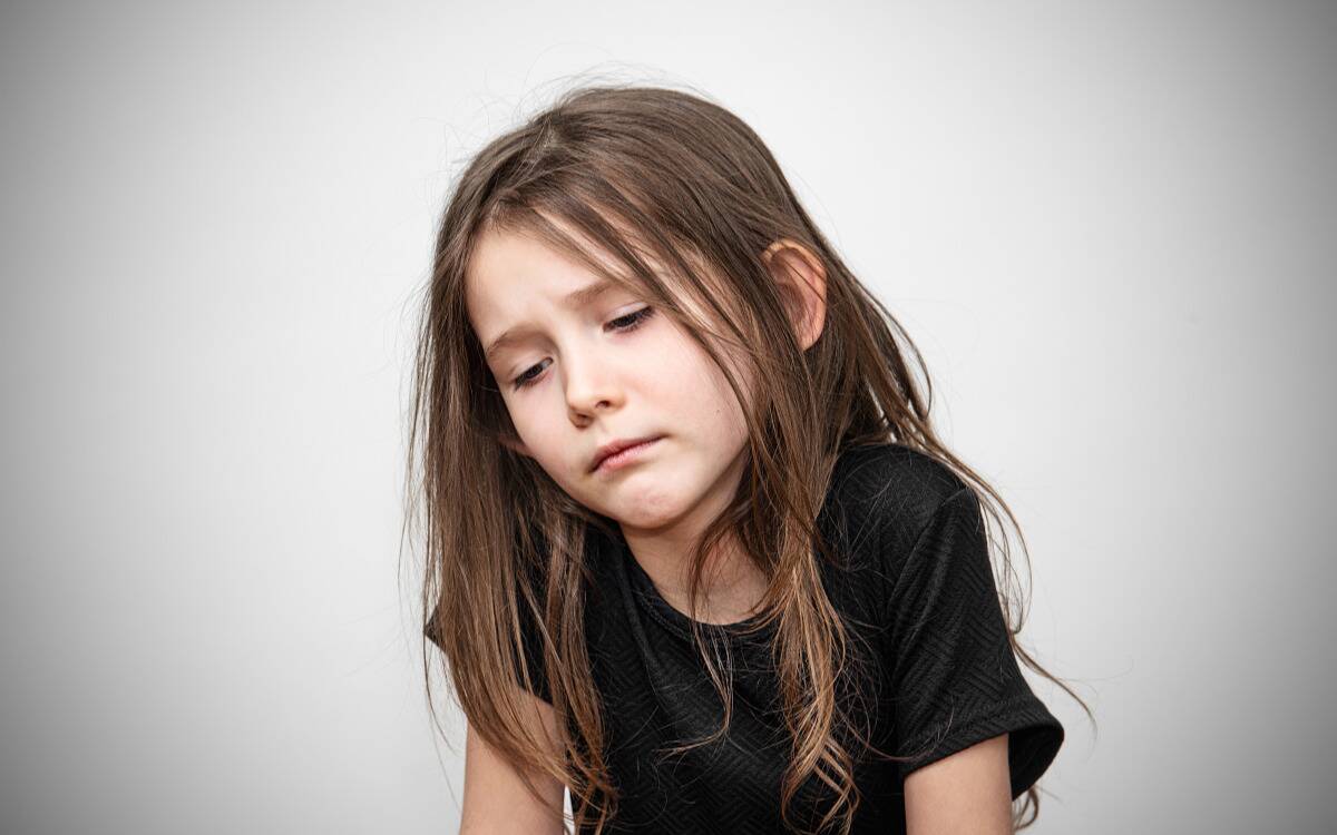A sad little girl in front of a grey backdrop.