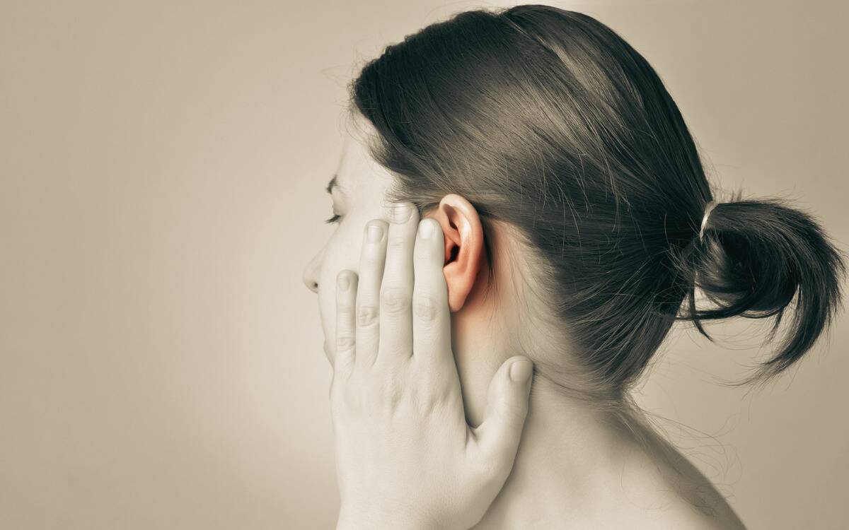 A sepia image of a woman with a hand raised to her cheek, her ear highlighted.