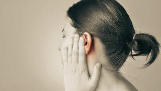 A sepia image of a woman with a hand raised to her cheek, her ear highlighted.