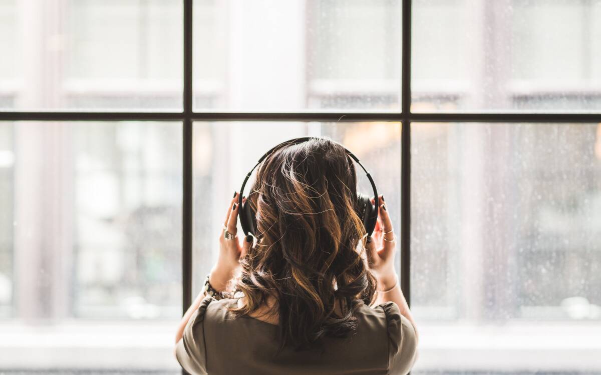 A woman standing in front of a large window putting headphones on.