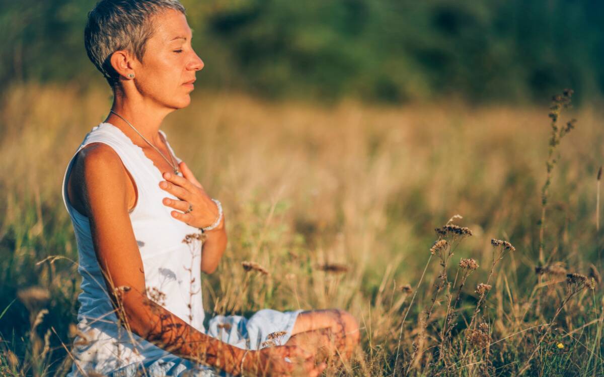 A woman meditating outside in a field, a hand over her chest.