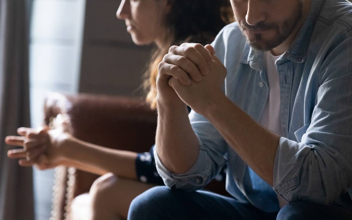 A couple sitting on a couch, facing away from each other, looking tense.