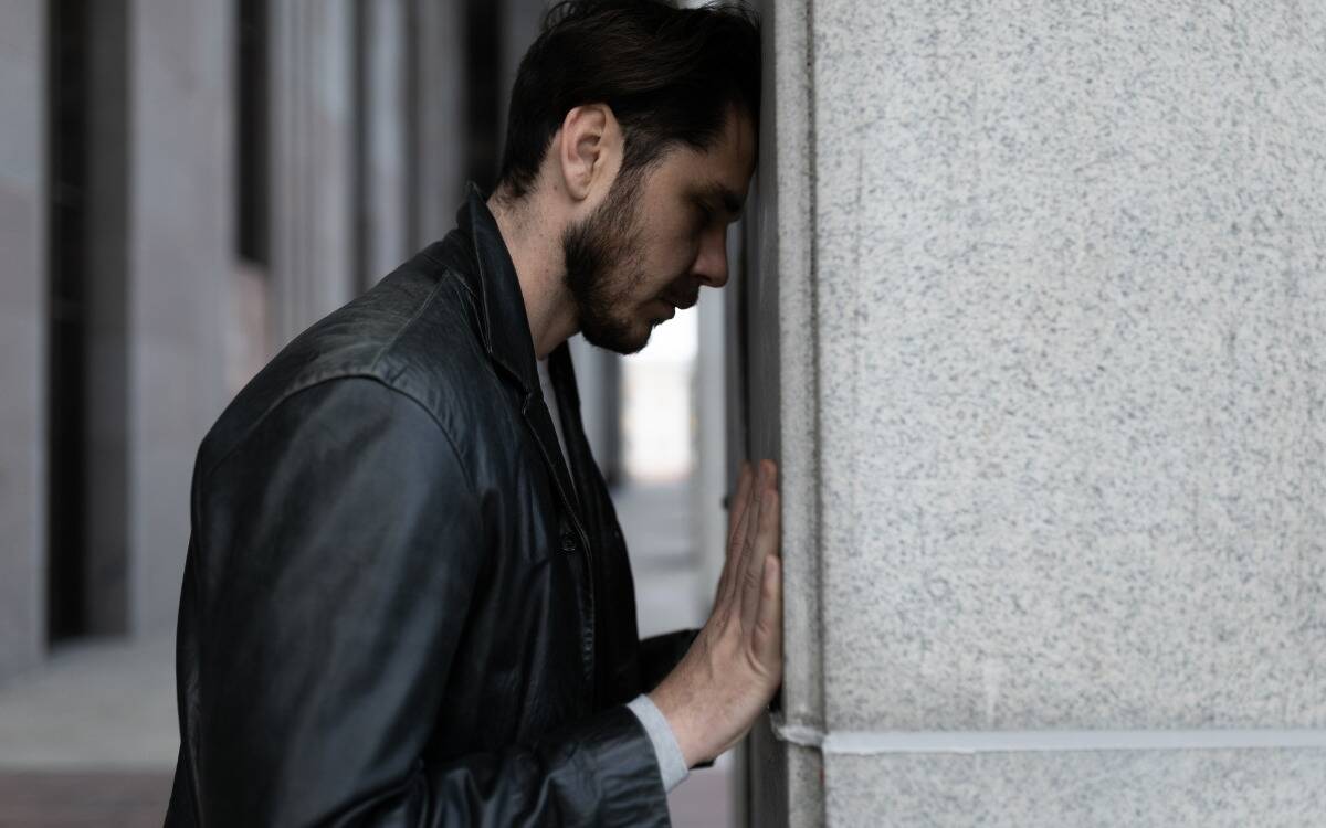 A man standing with his head and hands against a stone wall.