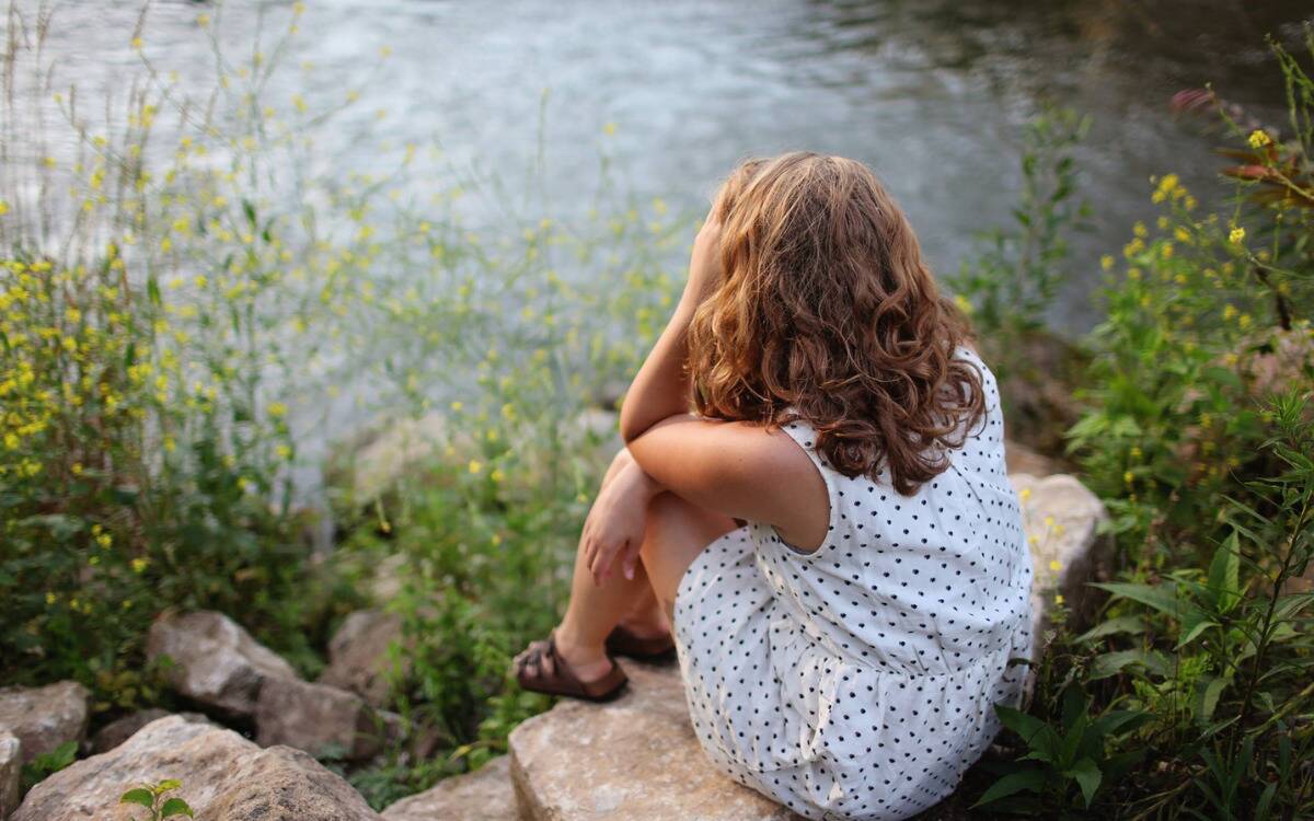 A woman sitting by the water contemplatively.