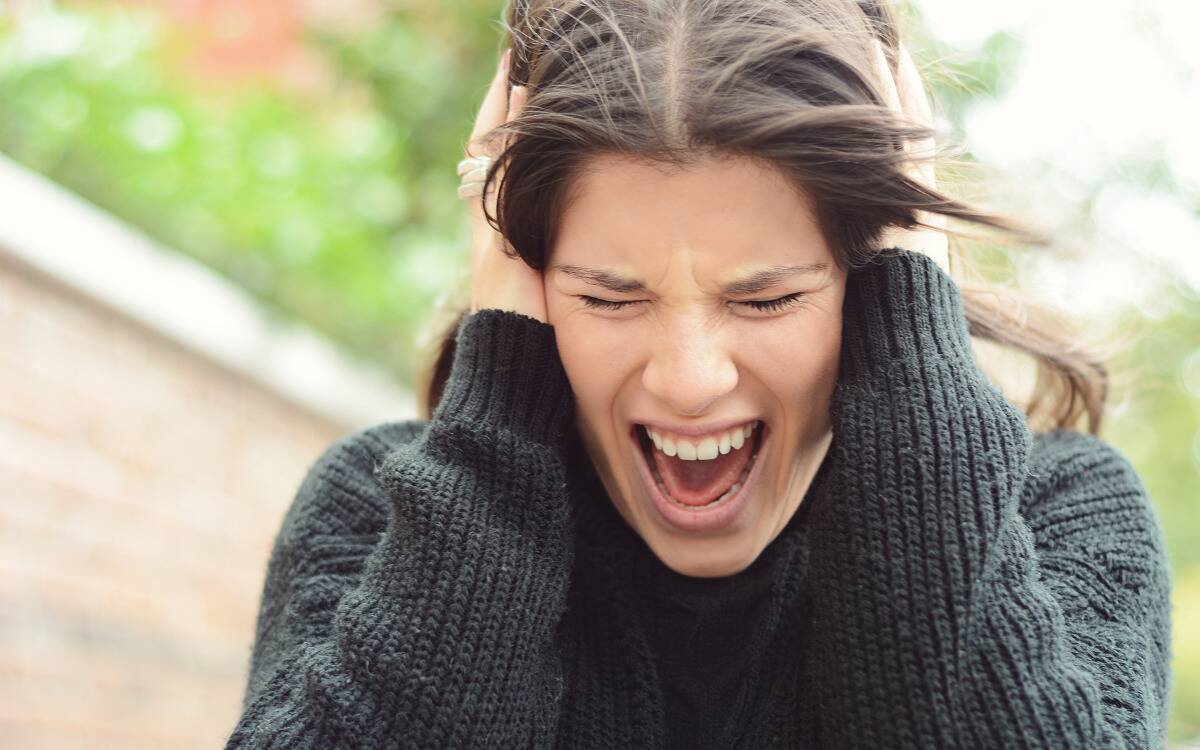 A woman yelling with her hands clutching her head.