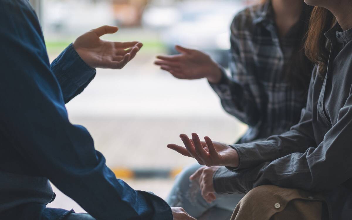 Three friends talking, each gesturing with their hands.