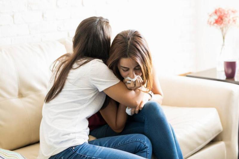 A woman hugging her friend who's actively crying into some tissues.