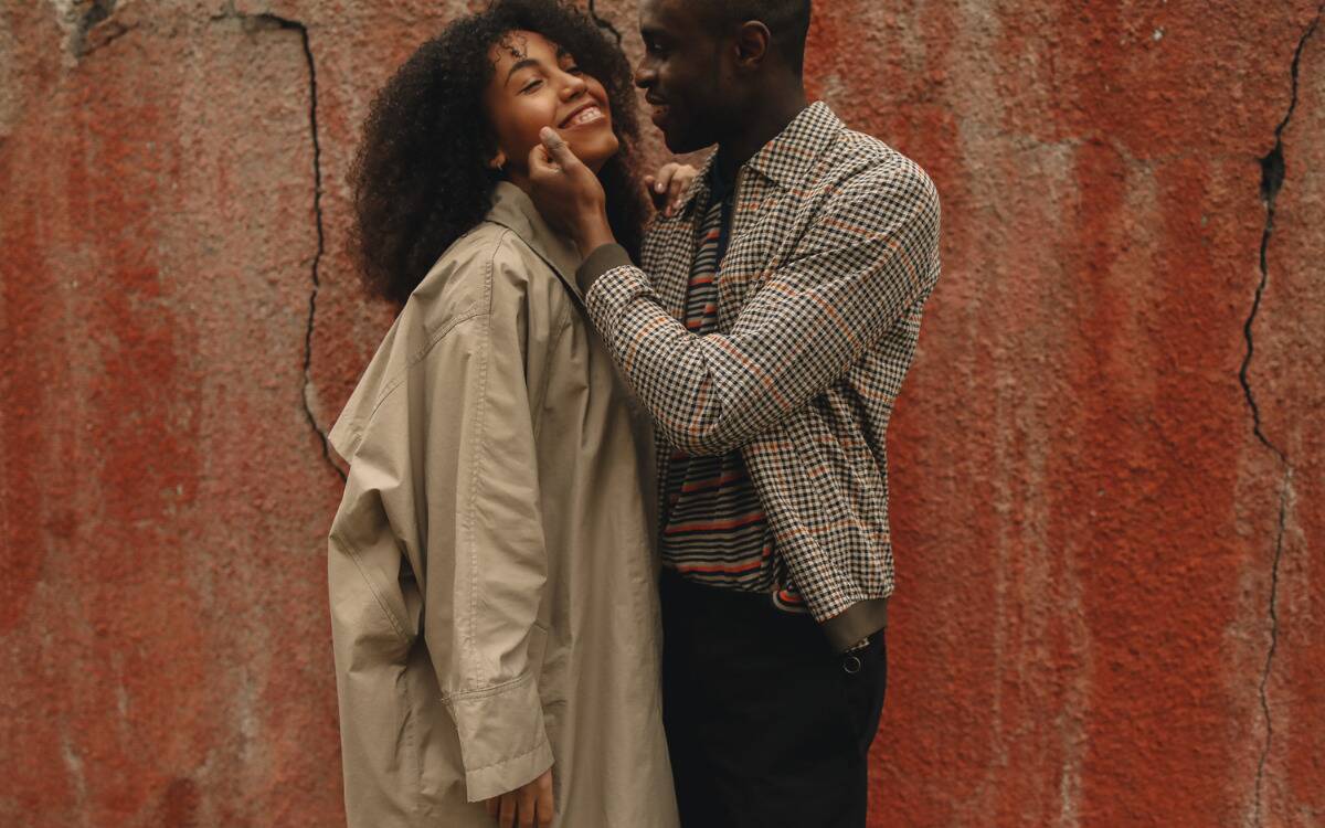 A couple standing close to one another, the man raising a hand to caress the woman's face.