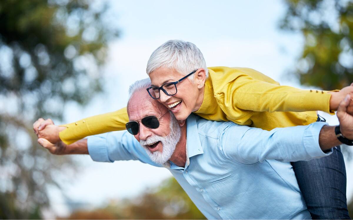 A woman balanced against a man's back, leaning forward and arms out in a dual 'airplane' pose.