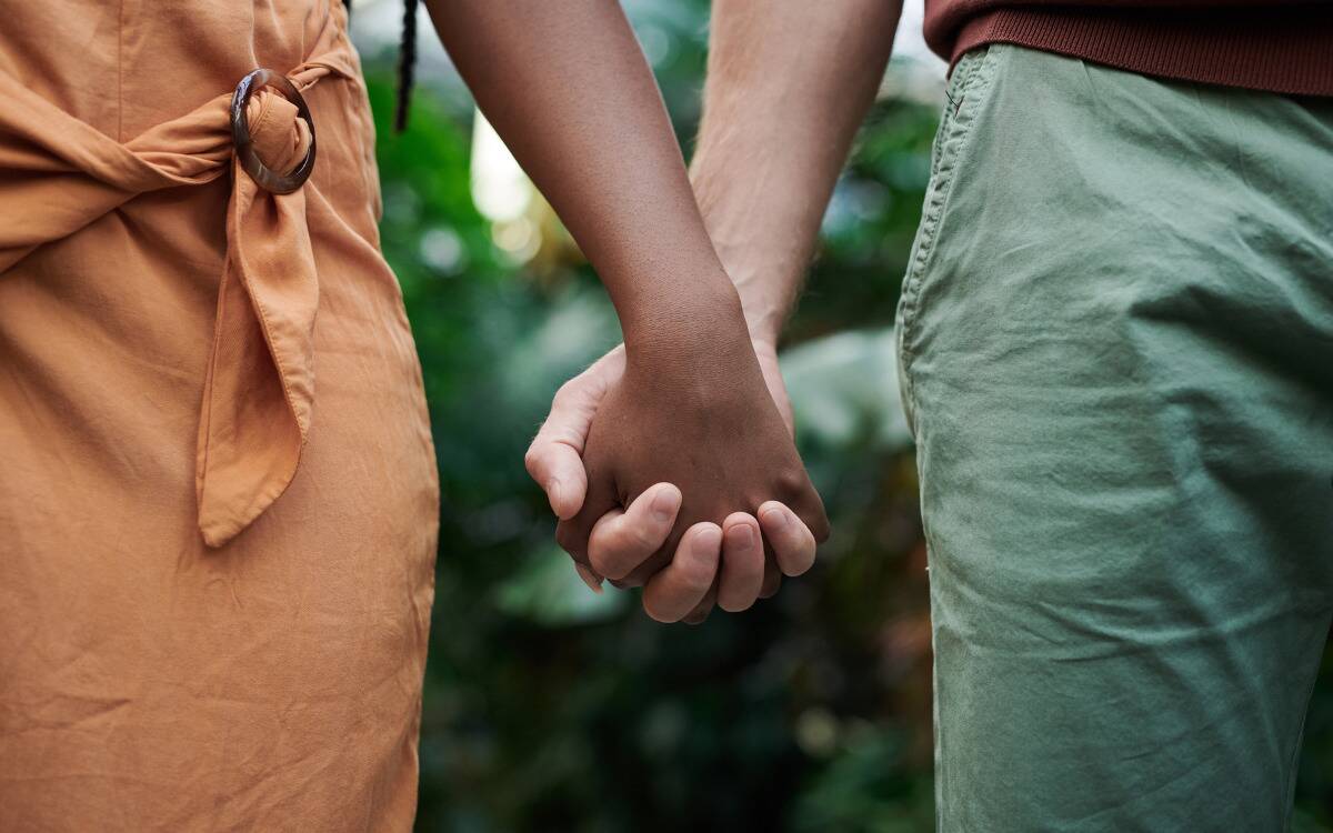 A closeup of a couple holding hands down at their sides.