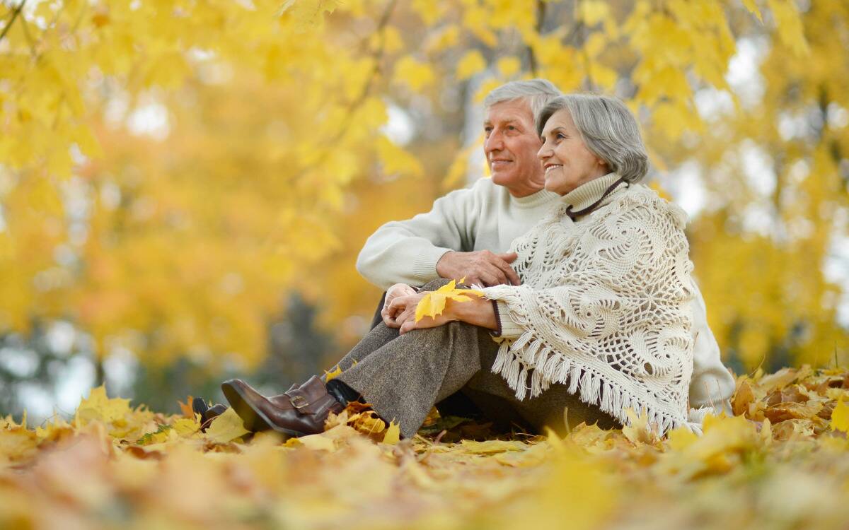 A couple sitting next to one another in the autumn fallen leaves.