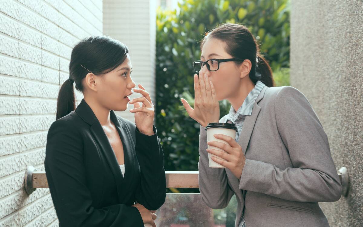 Two women in work attire gossiping.