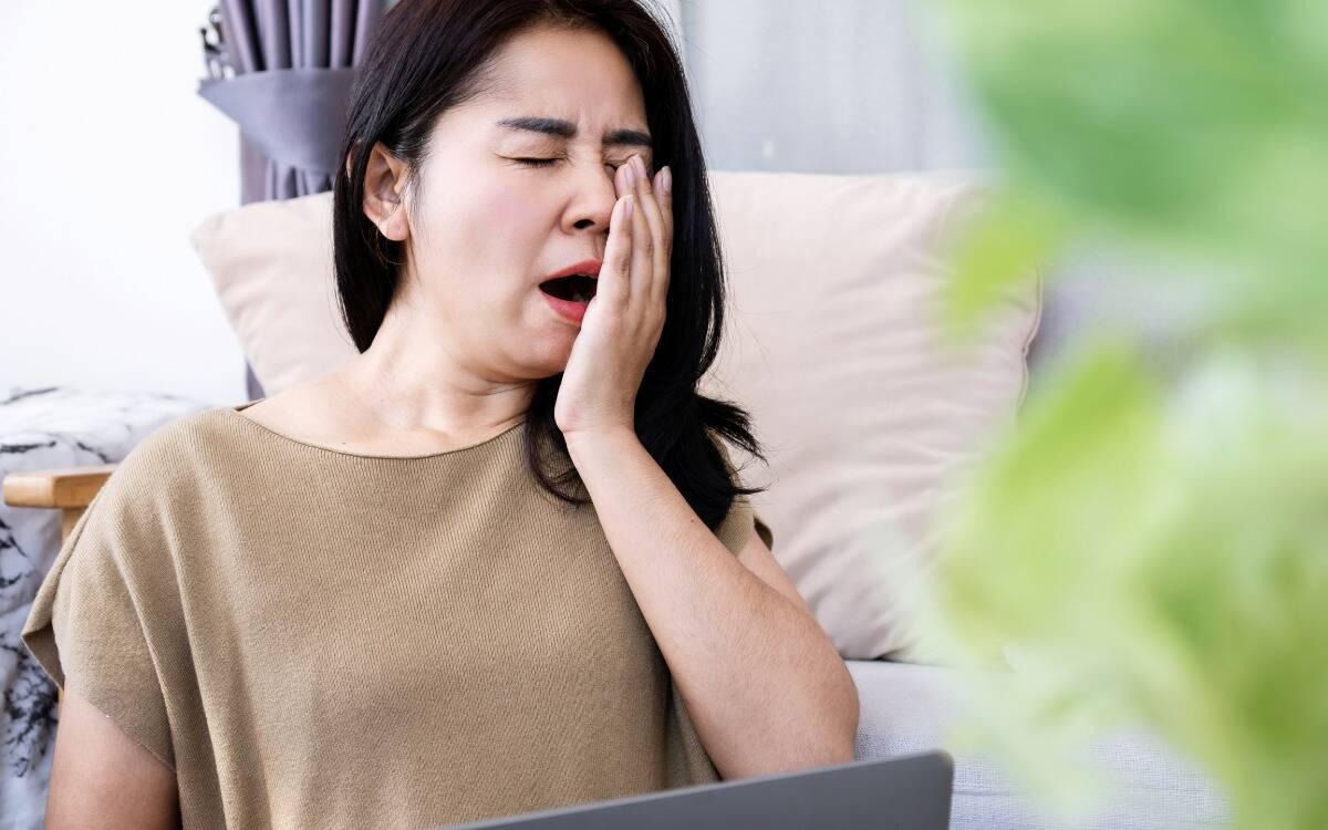 A woman yawning while sitting at her laptop.