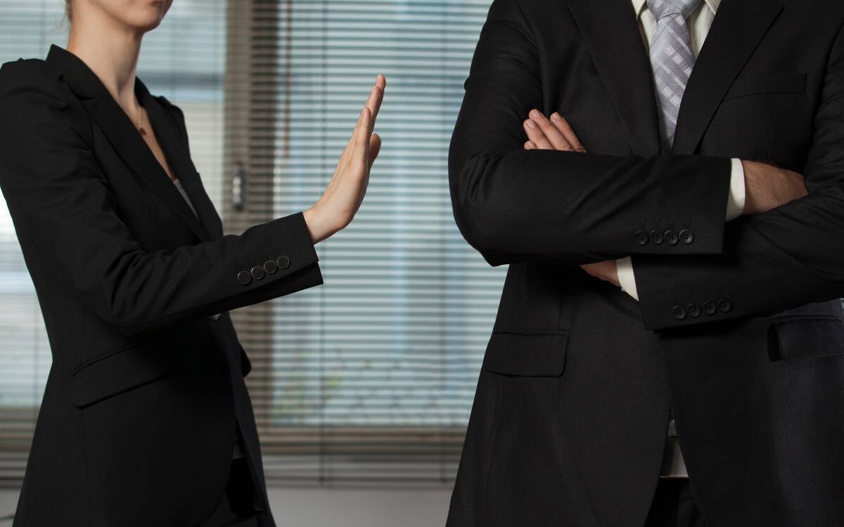 A woman holding up a 'no' sign with her hand toward her male coworker.