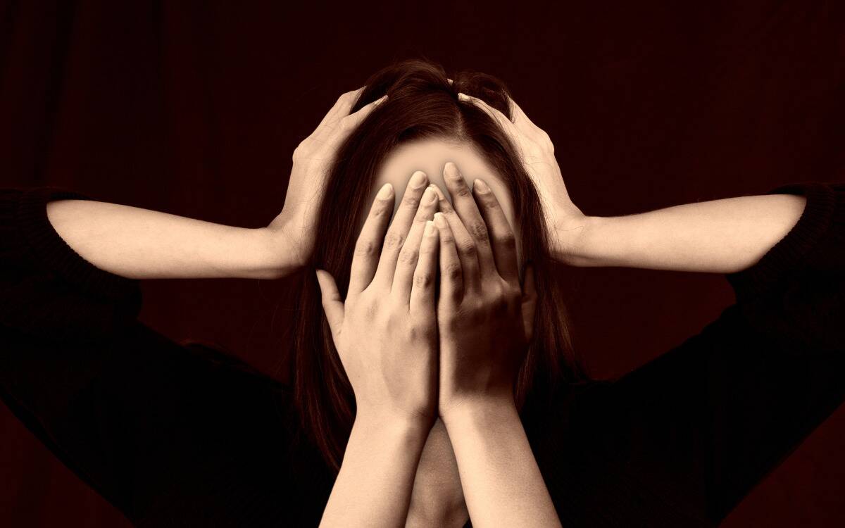 An image of a woman with two hands covering her face and two hands clutching the sides of her head.