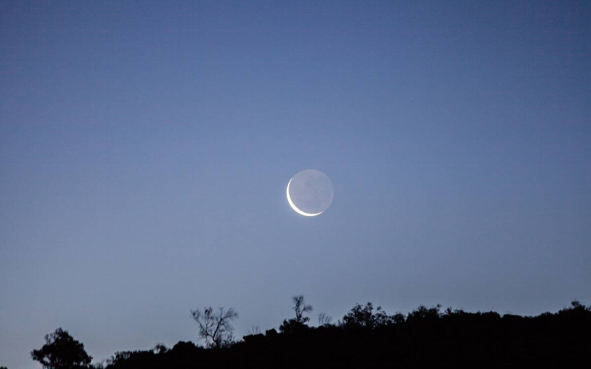 The new moon glowing in a light blue sky.