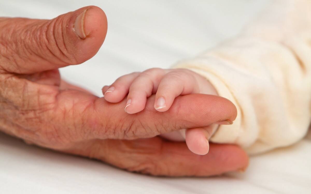 A small, baby's hand holding the finger of an elderly person.