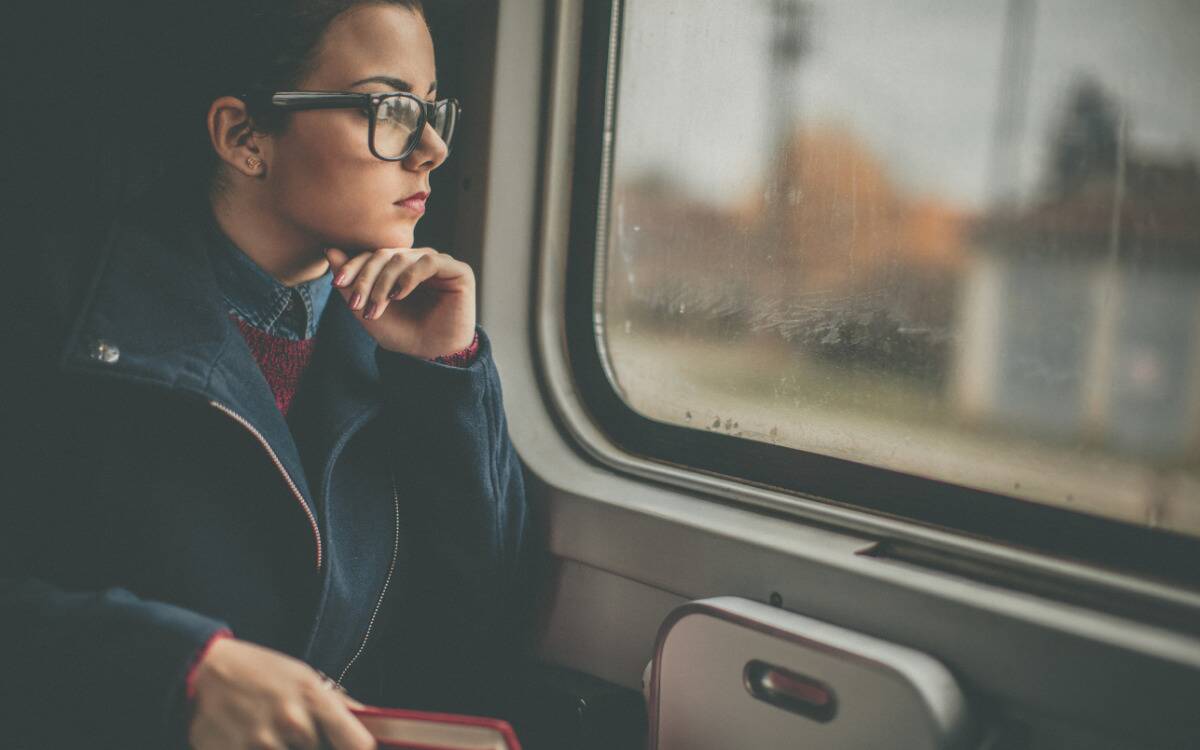 A woman looking pensively out a train window.