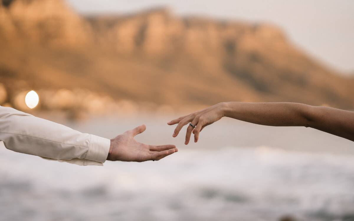 Two hands reaching out for one another in front of a natural landscape.
