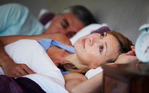 A woman awake in bed while her husband sleeps next to her.
