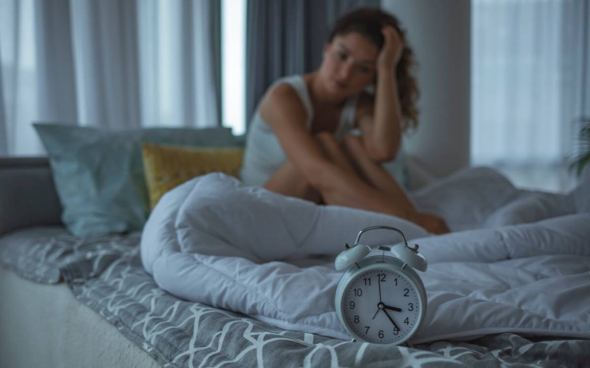 A woman awake in bed, staring at her clock that reads roughly 3:25 AM.