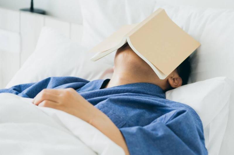 Someone asleep in bed with a book over their face.