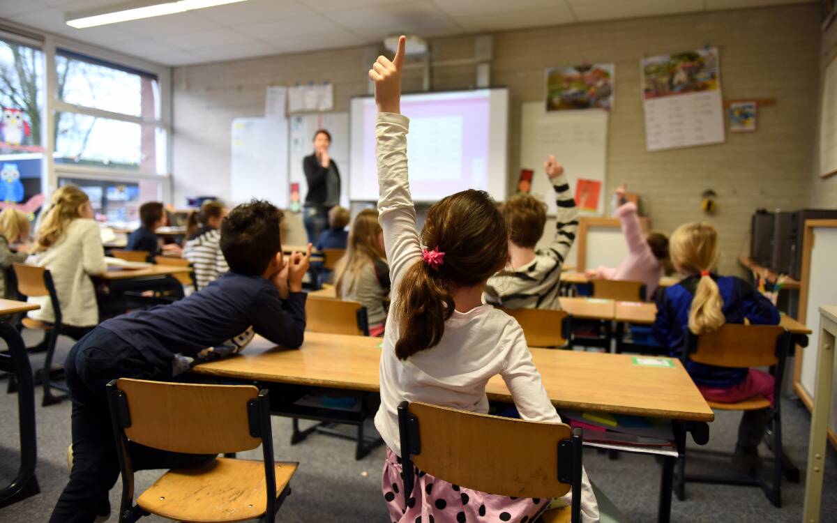 A classroom full of kids, a few students raising their hand.