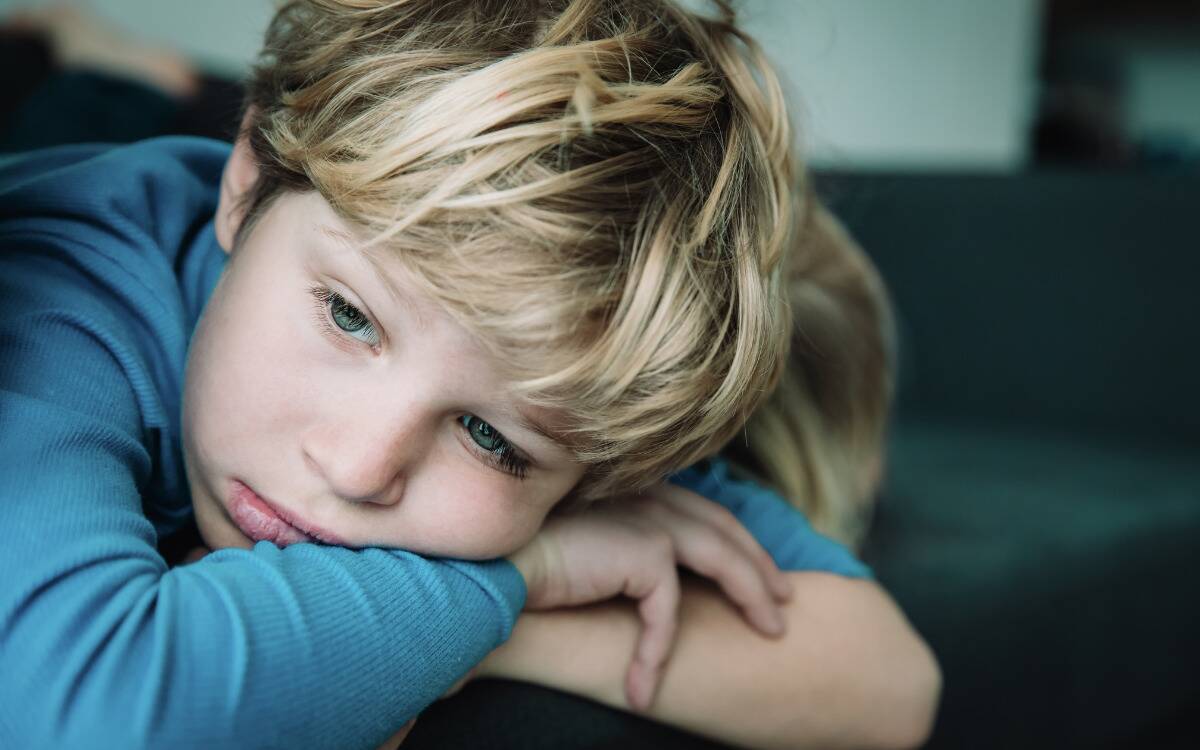 A young boy looking sad, laying his head on his folded arms.
