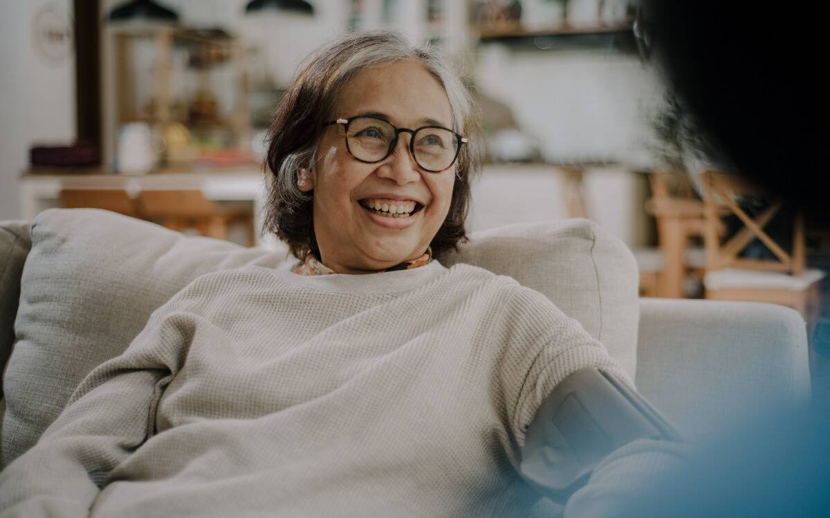 A woman smiling on her couch as she speaks to someone.