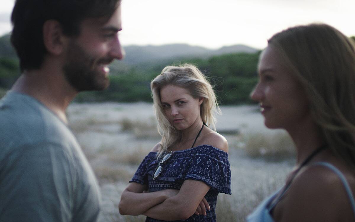 A woman watching a couple that's talking, looking jealous and bitterly at the woman.