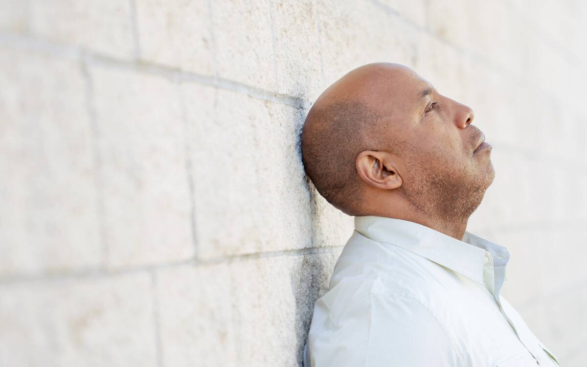 A man leaning his head back against a wall, looking sad.