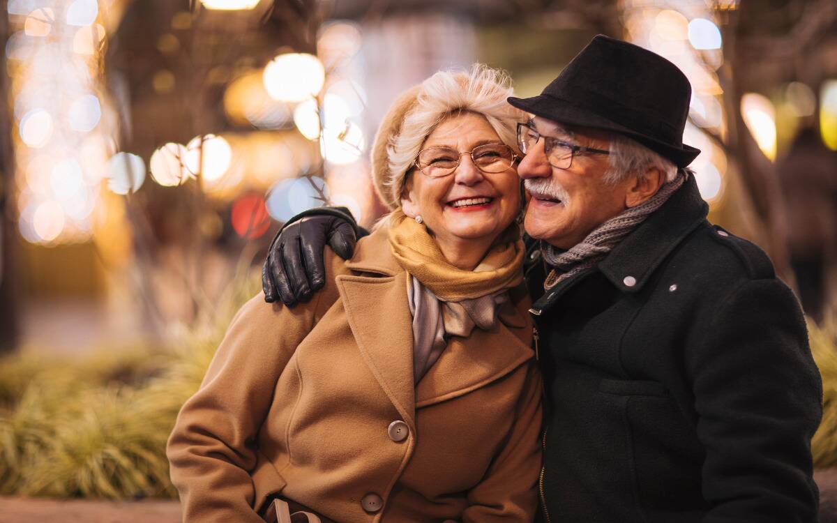 An older couple sitting on a bench outside, embracing.