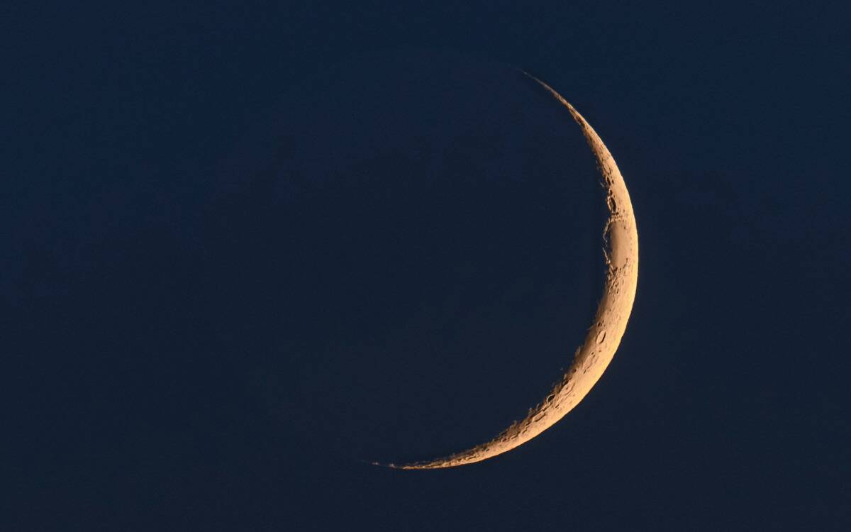 A yellowed waxing crescent moon large in the sky.