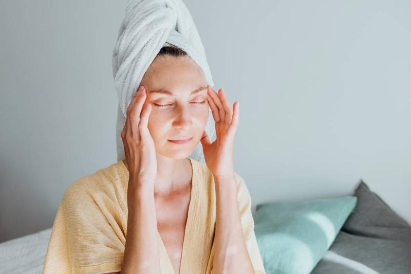 young woman with towel on head massaging her temples