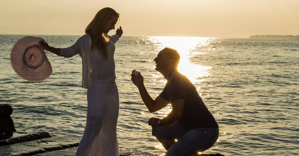 A man proposing to his wife on a boardwalk.