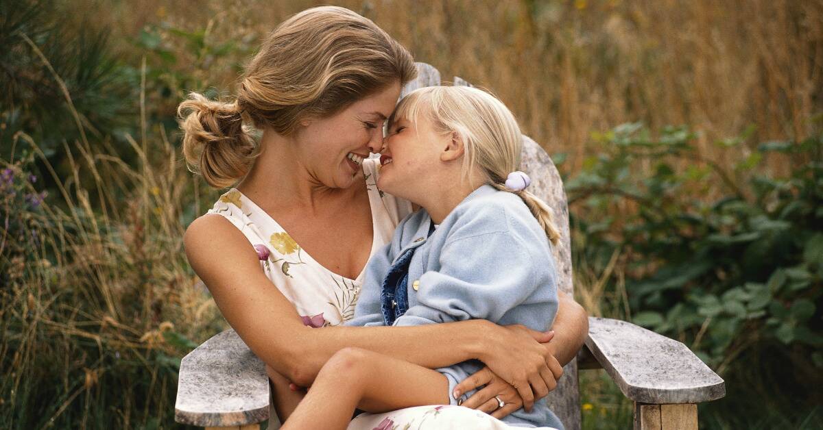 A mother and daughter sitting on a lawn chair, smiling as they lean in close to one another.