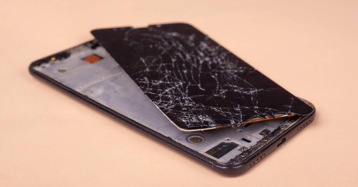 A cellphone with a shattered screen that has popped out of the frame.