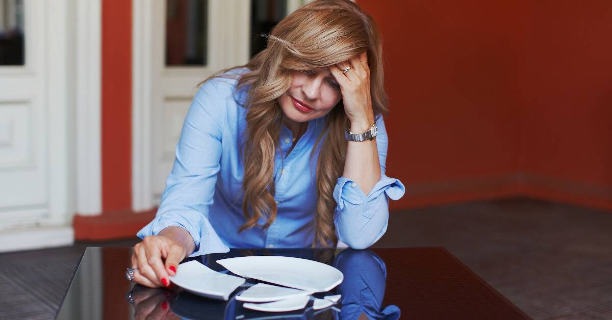 A woman sat at a table in front of a broken plate, looking disraught.