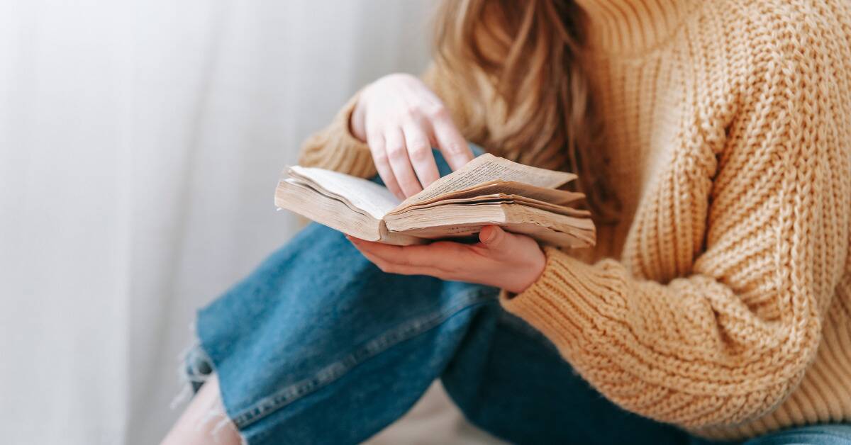 A woman in a cozy sweater reading an old book.