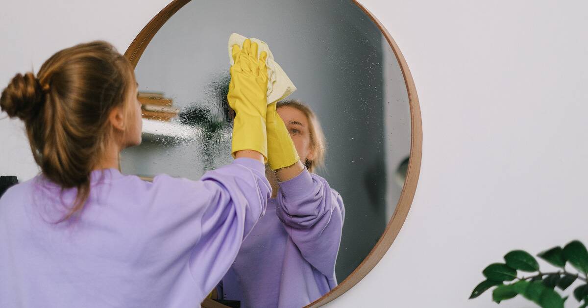 A woman cleaning a mirror with a rag.