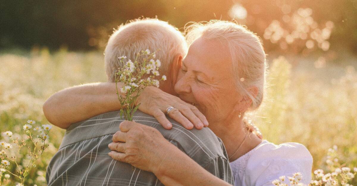 An older couple hugging, the woman holding a small bundle of wildflowers.