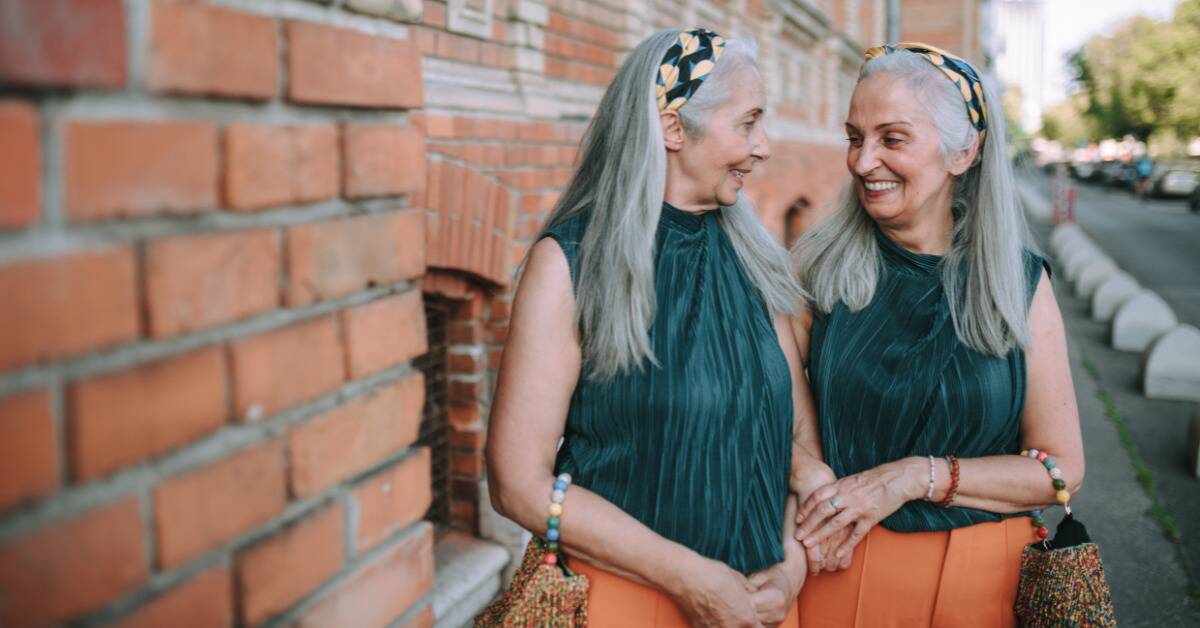 Two older women standing next to each other in matching outfits, smiling.
