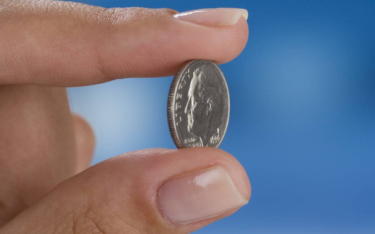 Someone holding a dime between their index finger and their thumb.