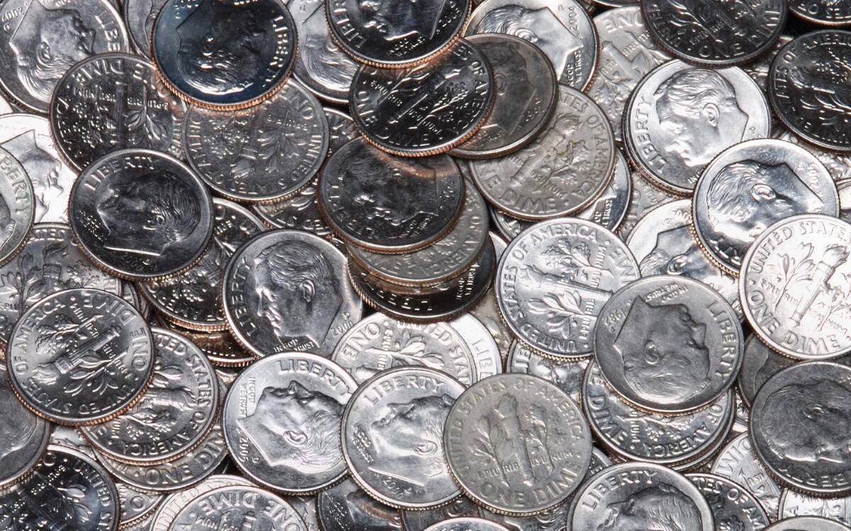A large quantity of dimes scattered about a table.