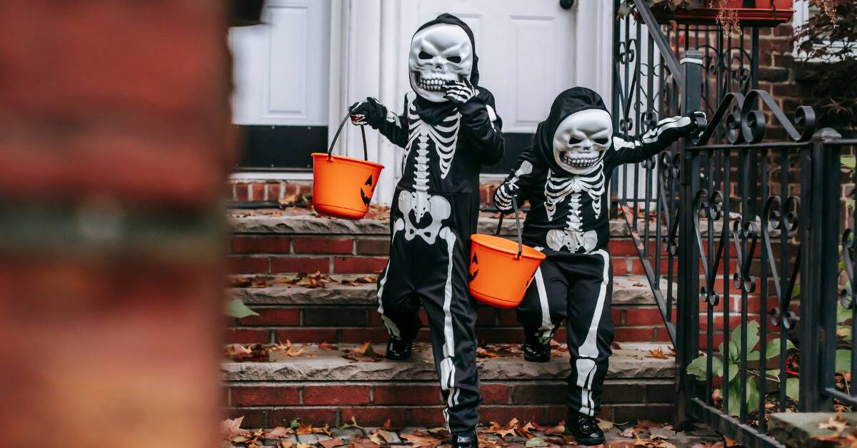 Two children in skeleton costumes walking away from a door after trick-or-treating.