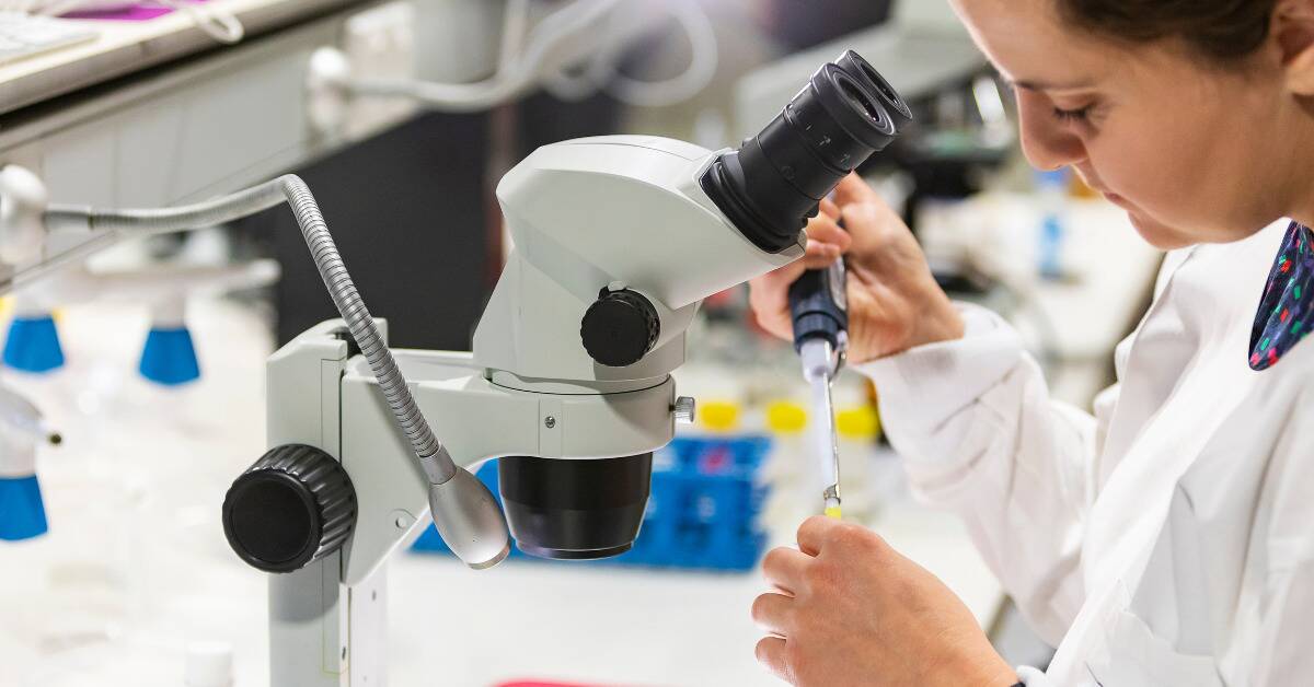 A closeup of a scientist doing research near a microscope.