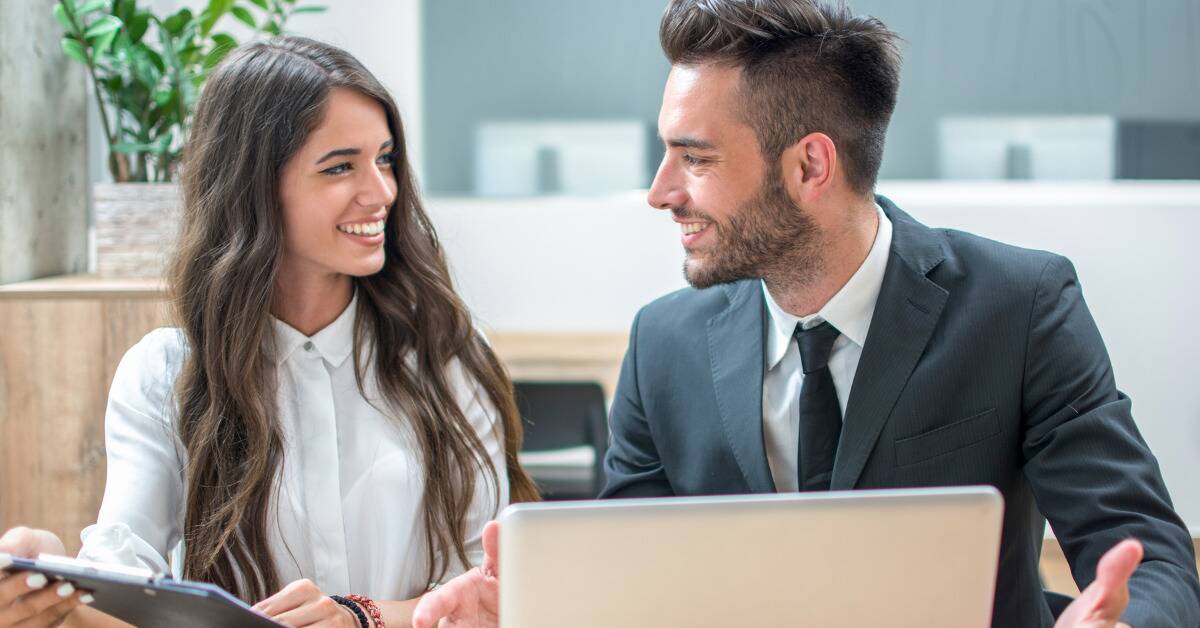 A man and a woman at work smiling as they chat.