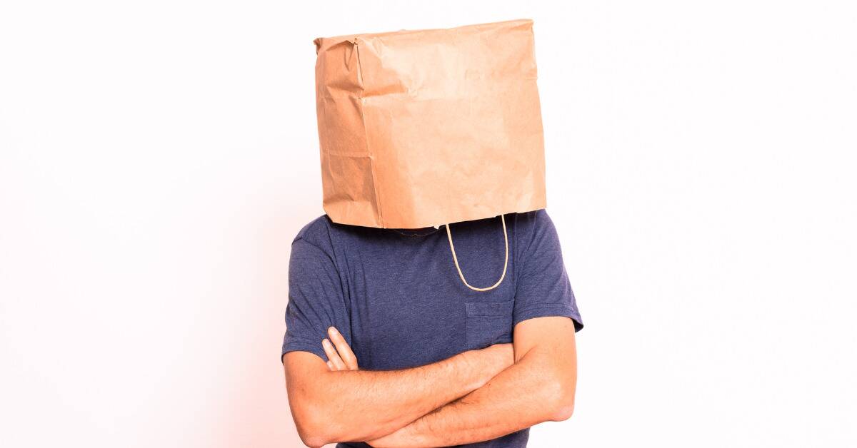 A man with his arms crossed and a paper bag over his head.